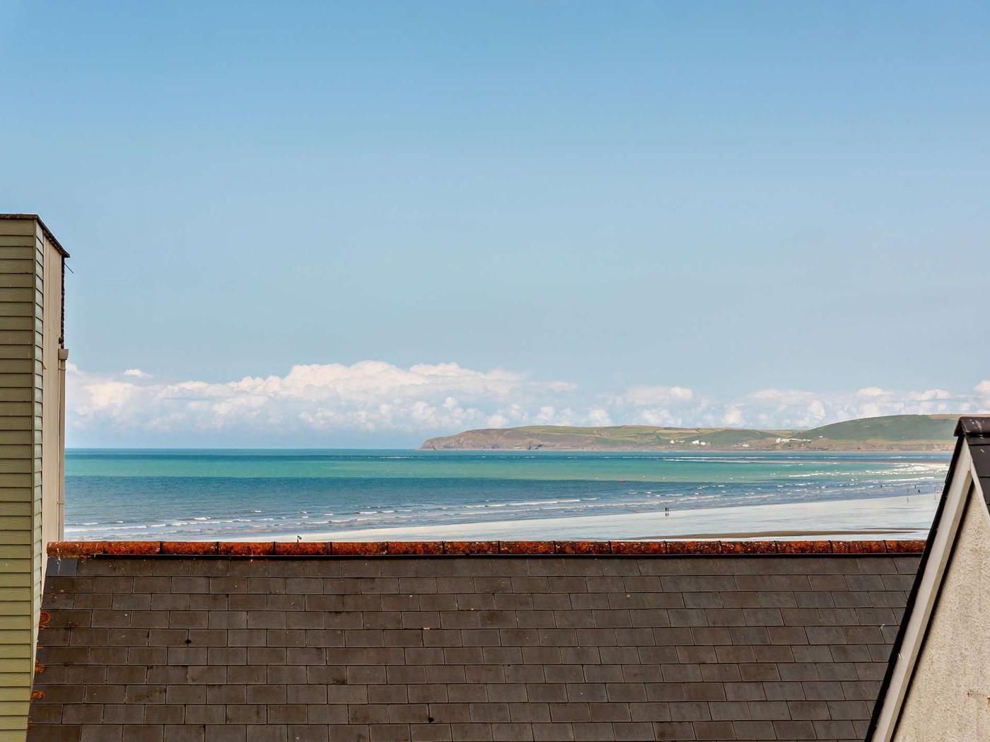 Vista costera desde una azotea con cielo despejado, una playa y colinas distantes.