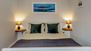 A bedroom with a bed, two bedside lamps, a framed picture above the bed, and a small table with a lamp. - 1 Bed in Ventnor (oc-91536) (Godshill)