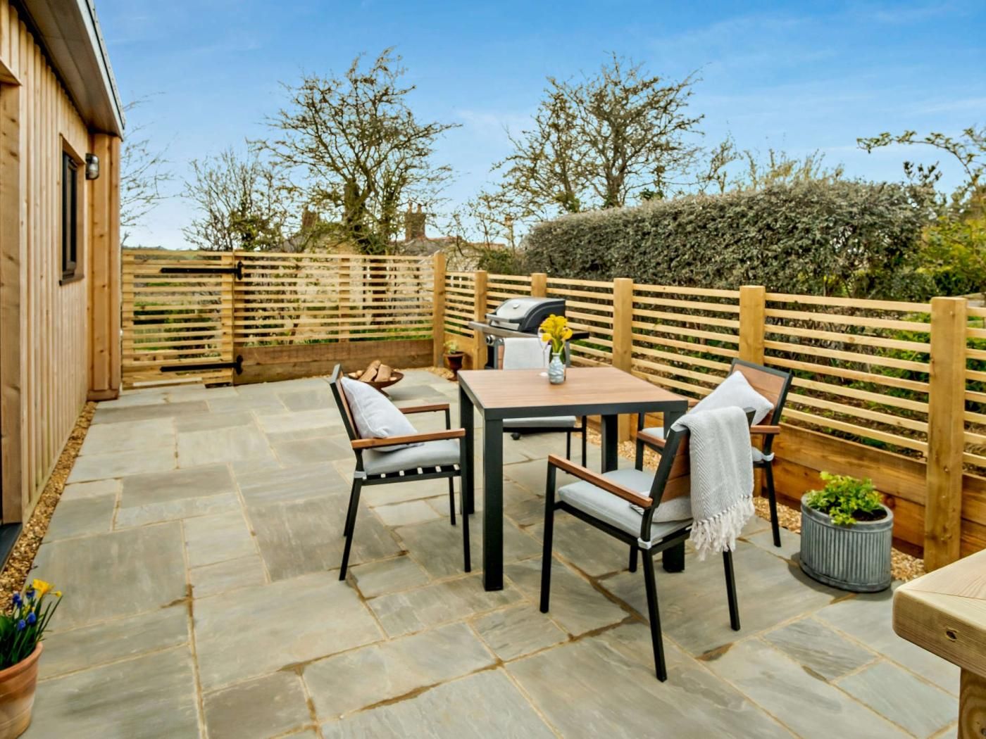 A patio with stone flooring, wooden furniture, and a wooden fence.