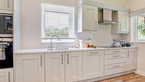 Eine moderne Küche mit weißen Schränken, einem eingebauten Backofen, einem Fenster mit Jalousien und einer Arbeitsplatte mit einer Brotdose und Küchenutensilien.