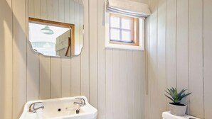 Un baño con lavamanos blanco, espejo, ventanal pequeño y planta en maceta.