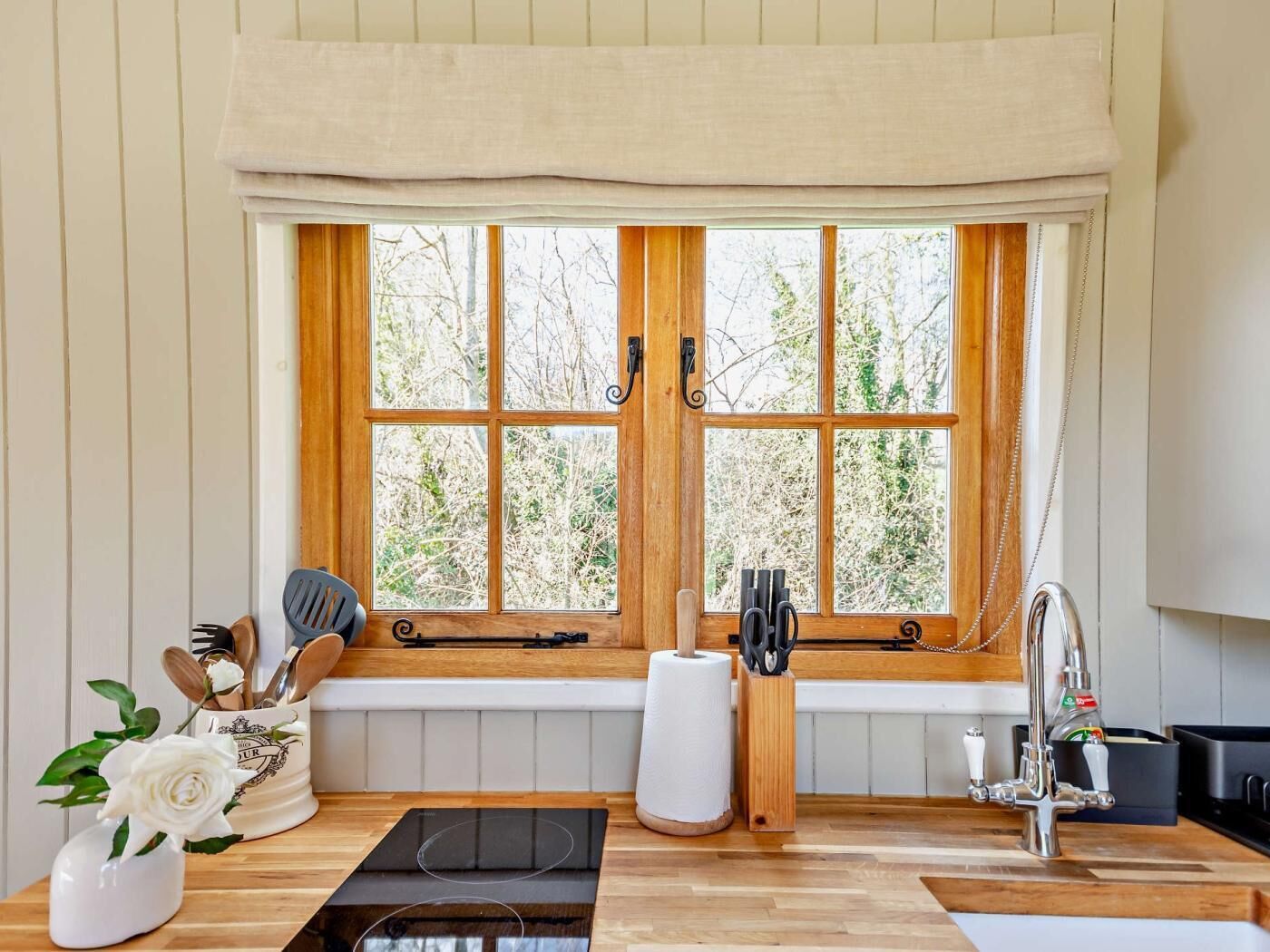 Eine Küche mit großem Fenster, Holzschränken und einer Arbeitsplatte mit verschiedenen Küchenutensilien.