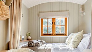Un dormitorio con cama, ventana con cortinas, mesita de noche con lámpara y una silla.