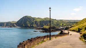 A coastal pathway with a stone wall, a lamp post, and a view of the sea and hills. - 1 Bed in Ilfracombe (oc-91652) (Ilfracombe)