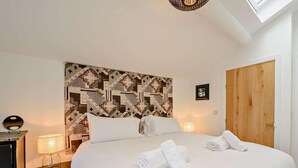 A hotel room with a large bed, a headboard with a geometric pattern, a wooden door, and a skylight. - 1 Bed in Ilfracombe (oc-91652) (Ilfracombe)