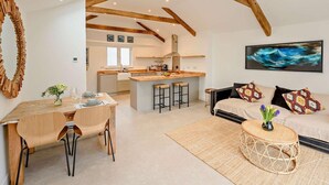 A spacious loft with exposed wooden beams, a kitchen with a central island, and a living area with a sofa and cushions. - 1 Bed in Ilfracombe (oc-91652) (Ilfracombe)