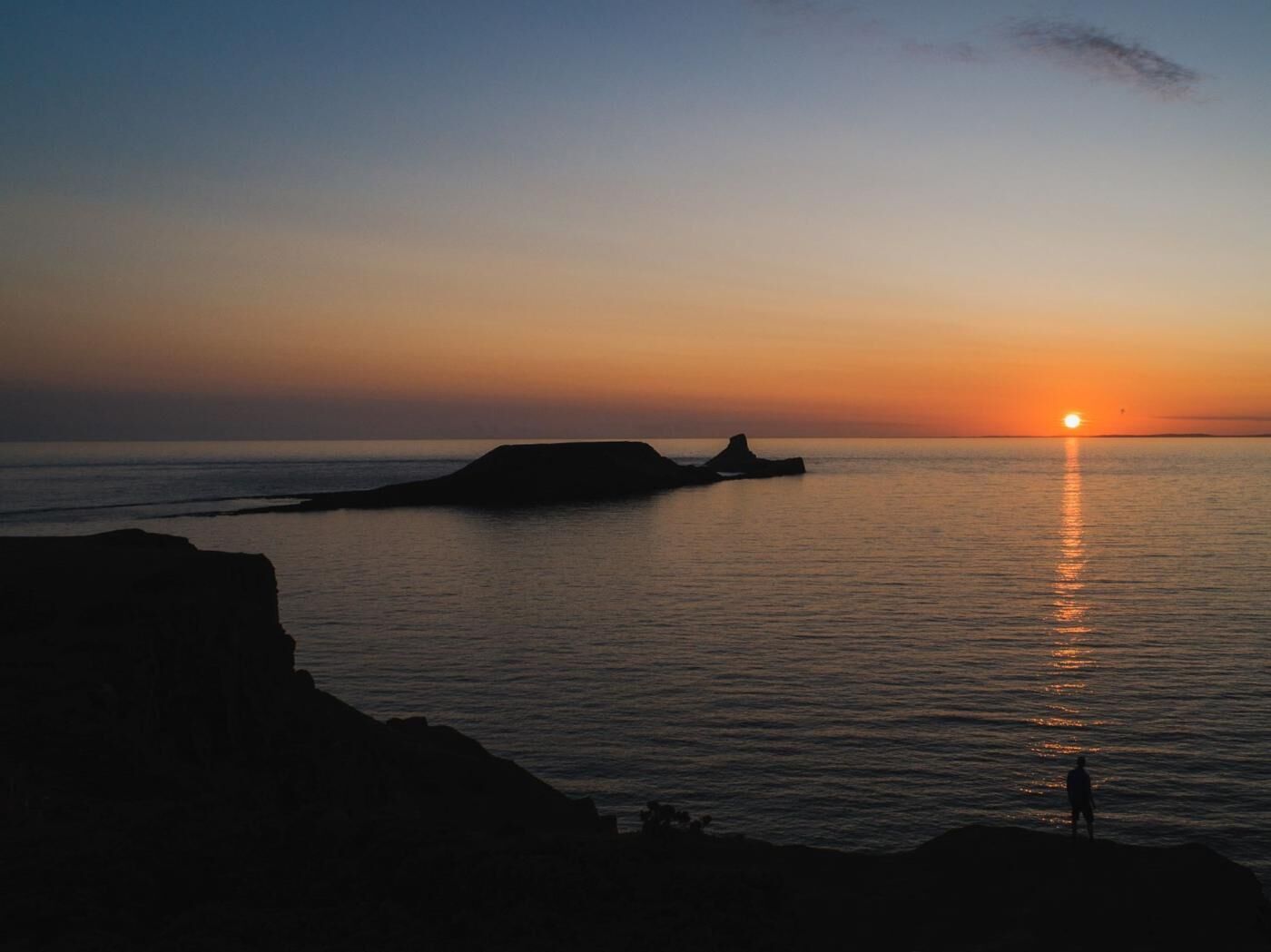 Un atardecer sobre un mar tranquilo con formaciones rocosas.