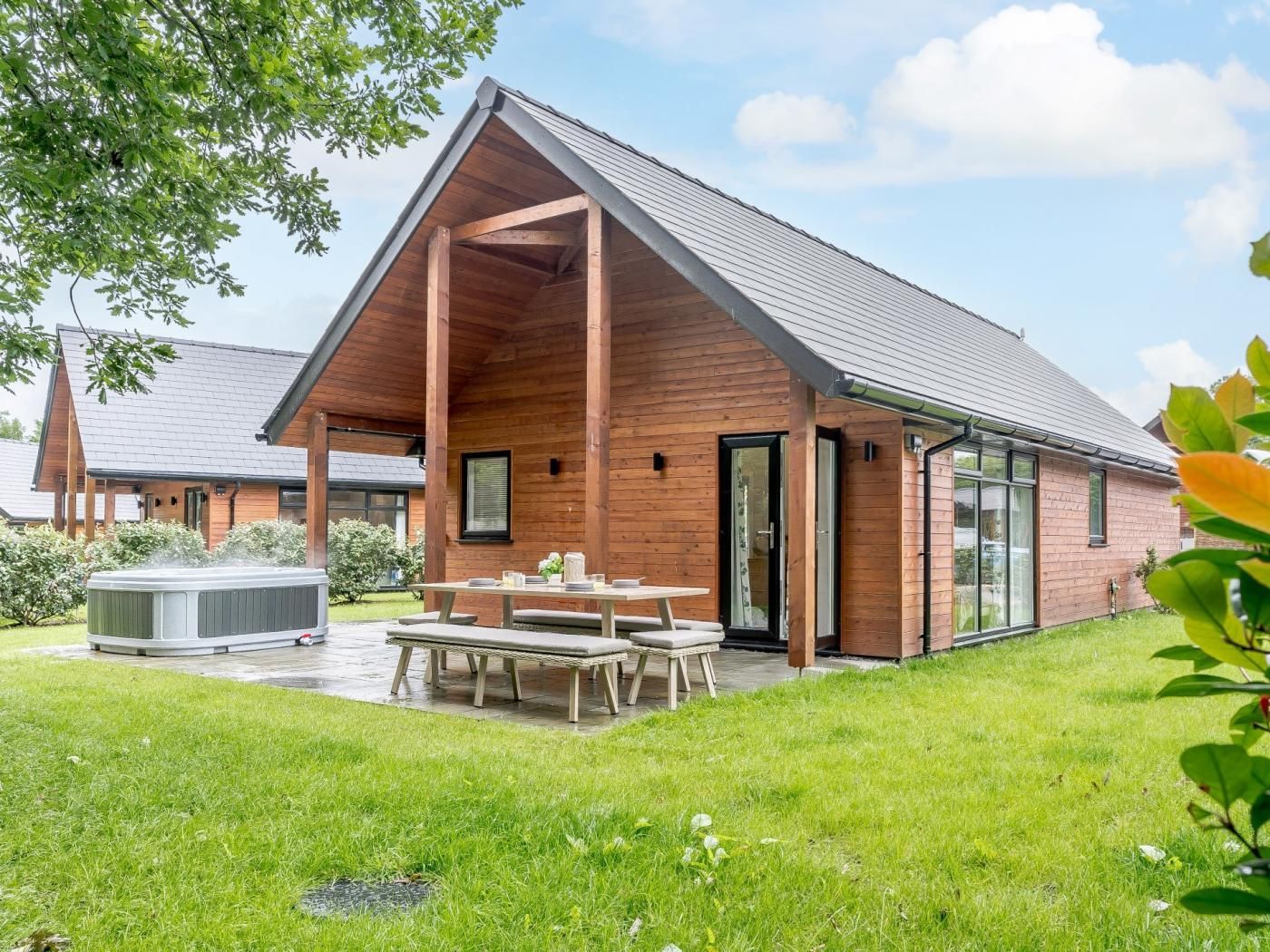 Een modern houten huis met een overdekt terras, een jacuzzi en een verzorgd gazon.