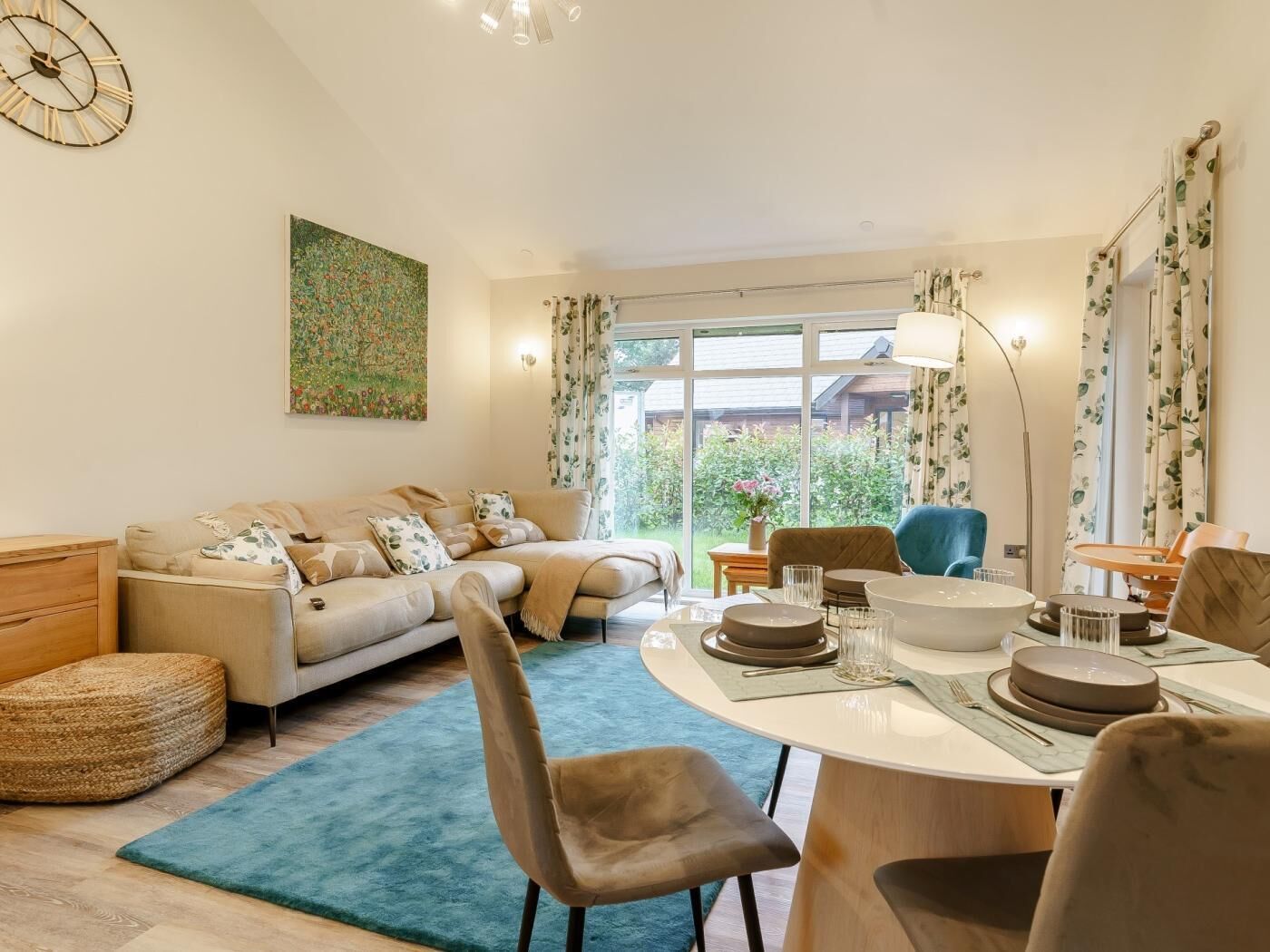 Uma sala de estar com sofá, cadeiras, mesa de jantar e uma grande janela com cortinas.