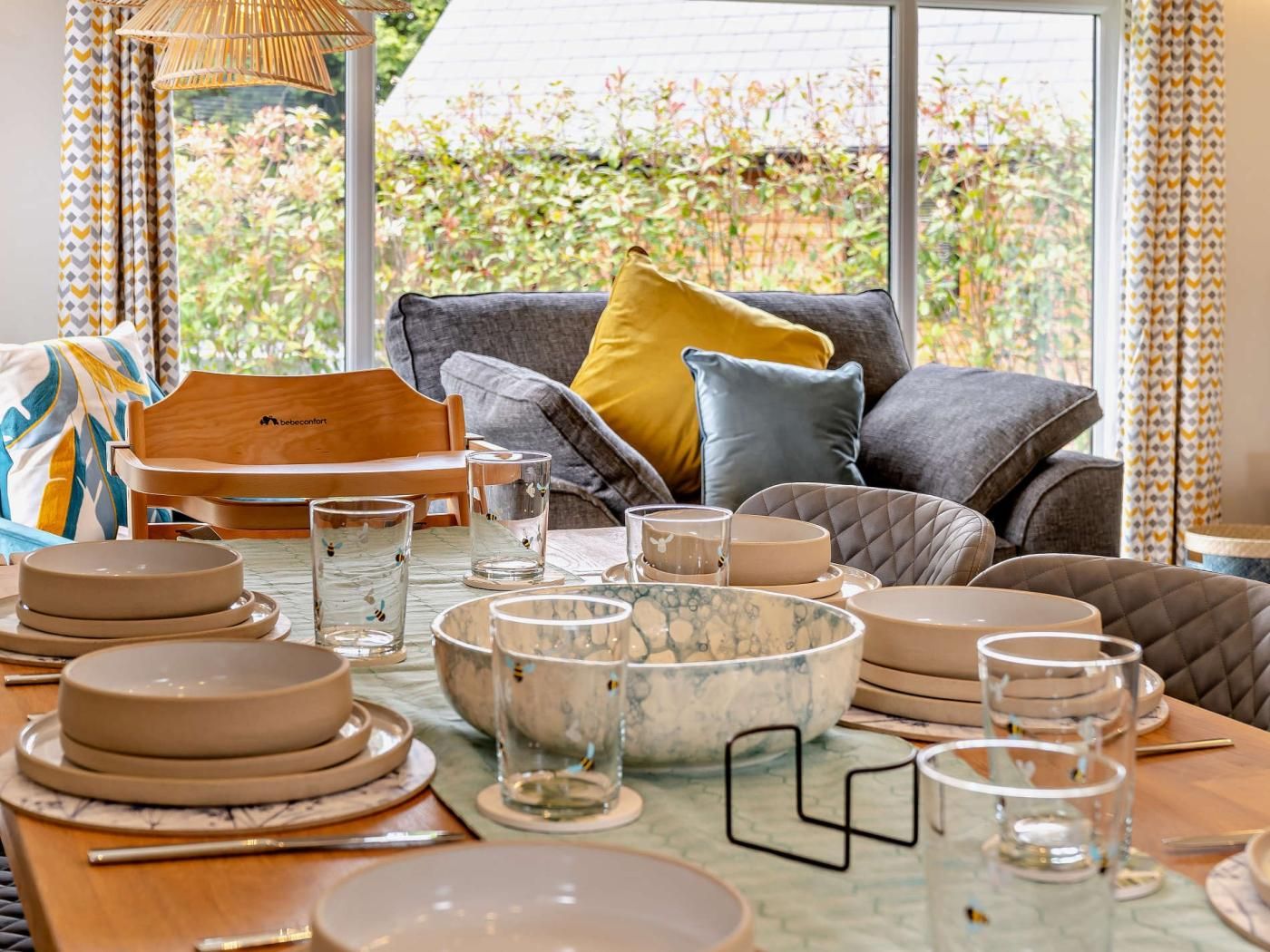 Un coin repas avec une table mise pour le repas, un canapé avec des coussins et une vue sur la verdure à l’extérieur.