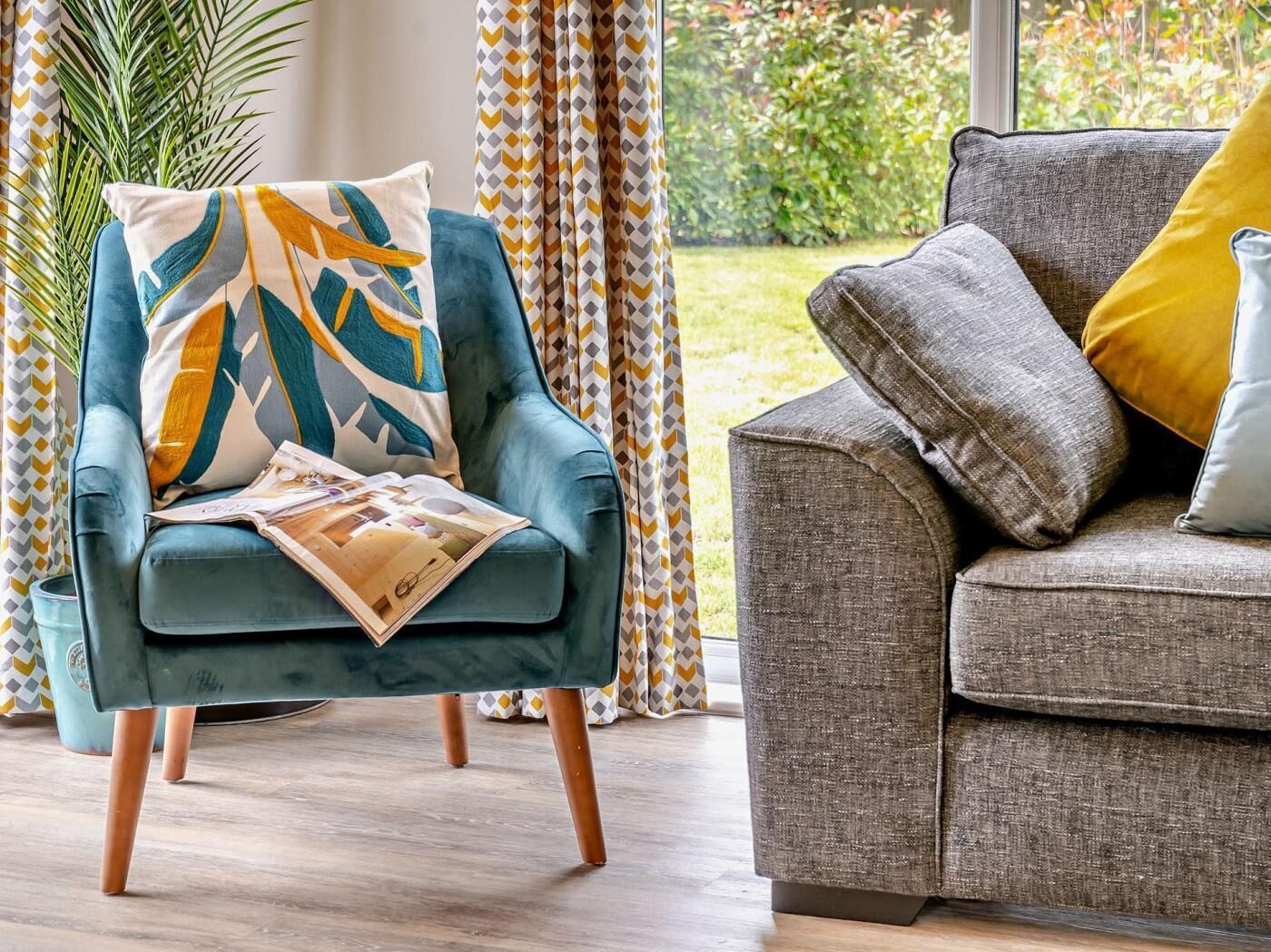 A living room with a blue armchair and a grey sofa, both with cushions.