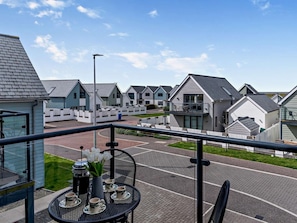 A balcony with a table set for tea, overlooking a row of modern houses with a clear sky above. - 2 Bed in Bideford (oc-91748) (Northam)
