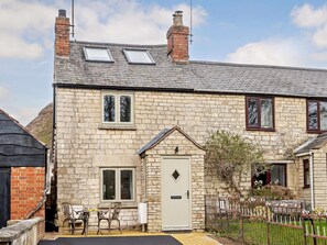 A stone house with a gabled roof, a front door, and a small porch with chairs. - 2 Bed in Gloucester (oc-91603) (Upton Saint Leonards)