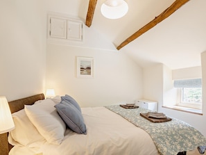 A bedroom with a bed, pillows, a nightstand, a lamp, a framed picture, a window with a view, and exposed wooden beams. - 6 Bed in Harlech (oc-91546) (Harlech)