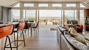 A spacious room with a large dining table, leather seating, and a view of the beach. - 3 Bed in Whitstable (oc-91641) (Seasalter)