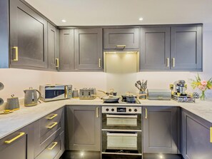 Eine moderne Küche mit grauen Schränken, goldenen Griffen und Edelstahlgeräten, darunter eine Kaffeemaschine und ein Backofen.