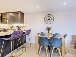 Una cocina moderna con armarios oscuros, una isla central con taburetes de bar y una zona de comedor con mesa y sillas de madera.