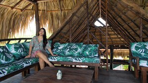 A thatched-roof structure with a wooden bench and a sofa with a tropical leaf pattern.