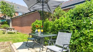 Een terras buiten met een tafel en stoelen, een picknicktafel, en een haag op de achtergrond.