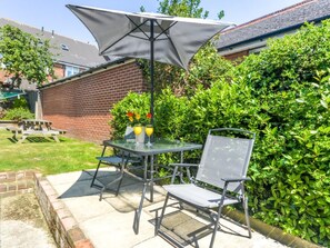 Eine Terrasse im Freien mit Tisch und Stühlen, einem Picknicktisch und einer Hecke im Hintergrund.