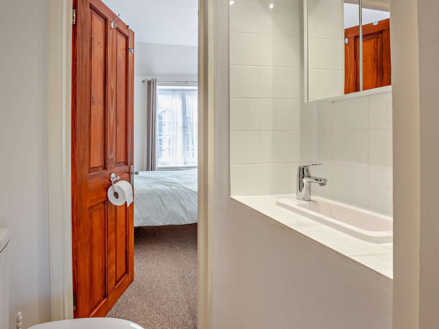 Un bagno con un lavandino bianco, uno specchio e una porta in legno.