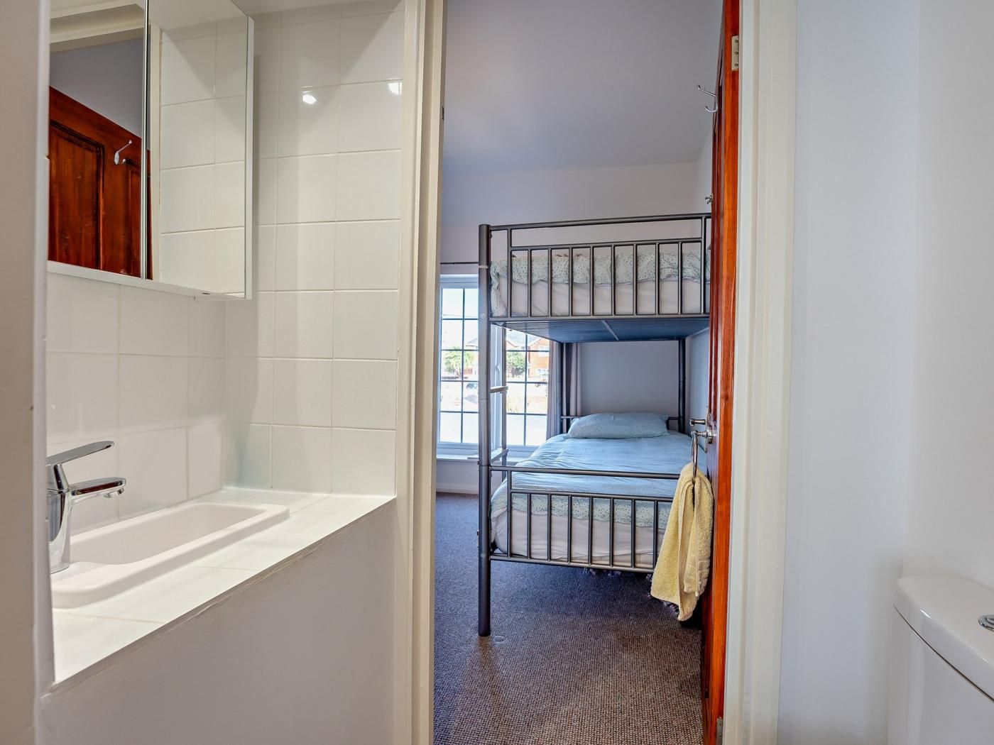 Een slaapkamer met stapelbed en een badkamer met wastafel en spiegel.