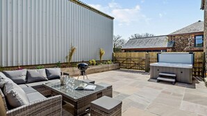 Eine Terrasse mit Gartenmöbeln, einem Grill und einem Whirlpool.