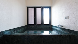 A bathroom with a large rectangular bathtub, a door with a window, and a wall-mounted faucet. - Del Mare Kiami (Masuda)