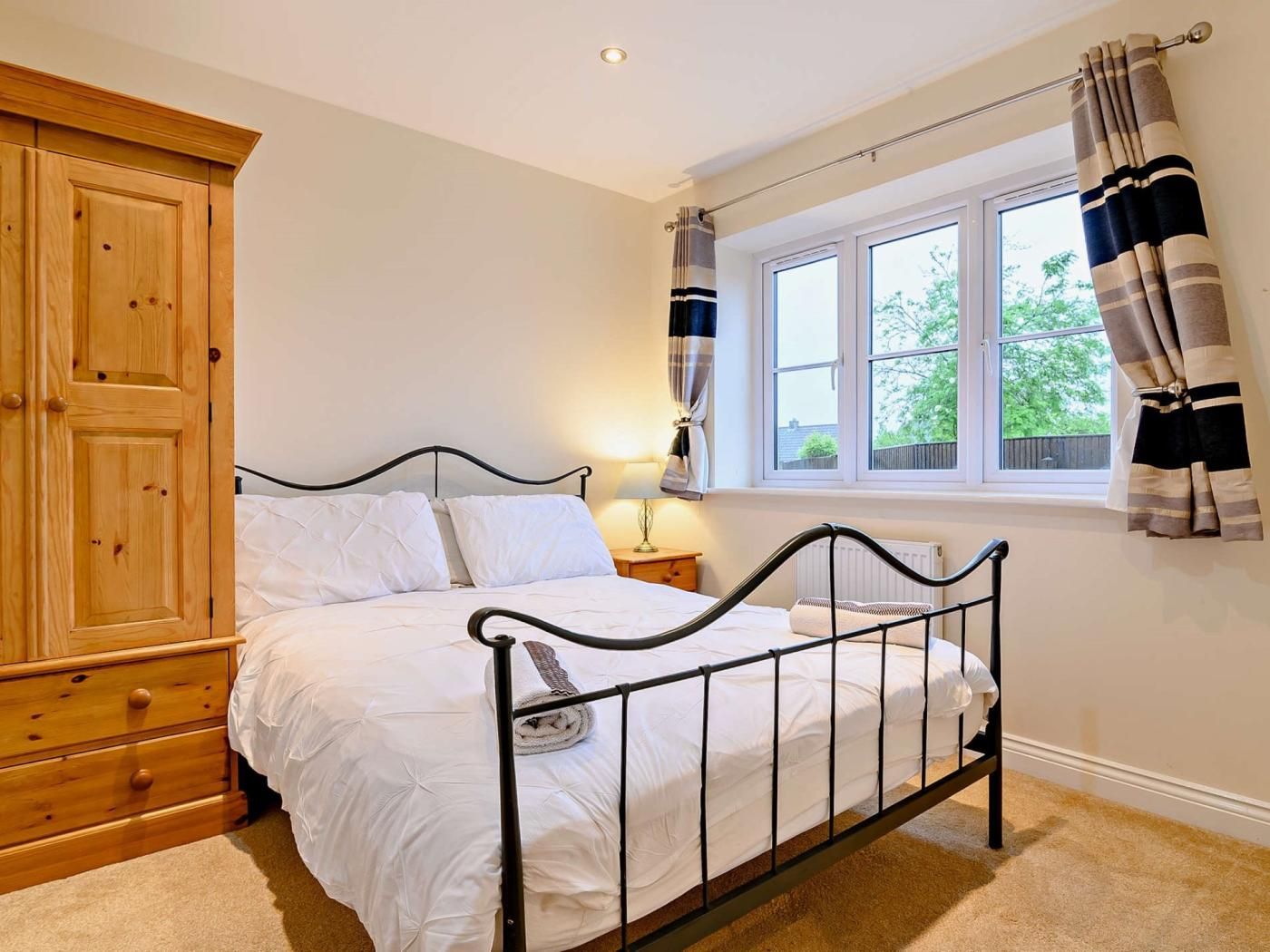 A bedroom with a bed, wooden wardrobe, window with curtains, and a lamp.
