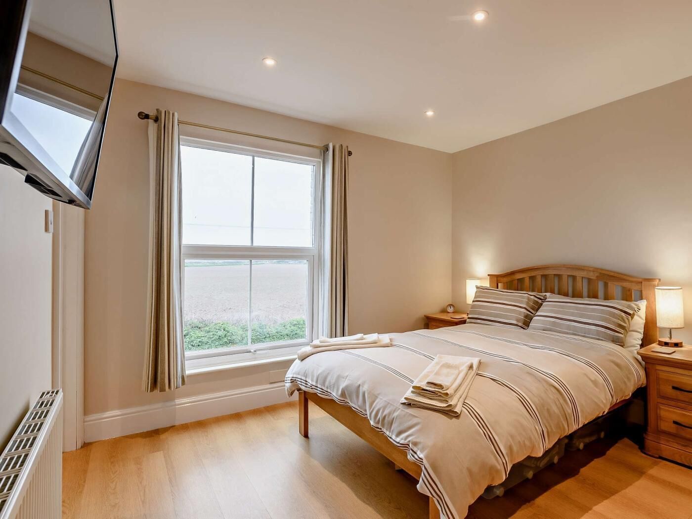 A bedroom with a bed, bedside tables, a TV, and a window with curtains.