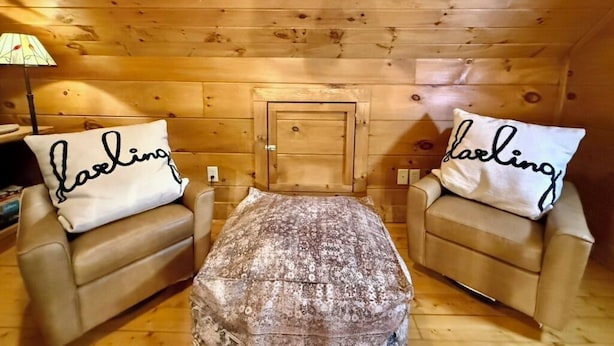 A cozy room with wooden walls, two leather sofas, and a patterned ottoman. - Boulder Lodge - The Perfect Mountain Escape in Banner Elk near Winery & Hiking (Banner Elk)