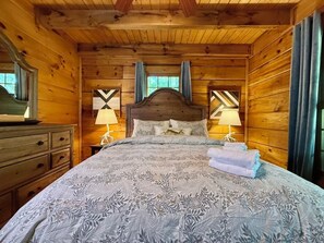 A wooden cabin bedroom with a bed, two bedside lamps, and a dresser. - Boulder Lodge - The Perfect Mountain Escape in Banner Elk near Winery & Hiking (Banner Elk)