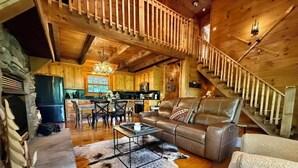 A cozy cabin interior with a wooden staircase, a dining area, and a living room with a leather sofa and a coffee table. - Boulder Lodge - The Perfect Mountain Escape in Banner Elk near Winery & Hiking (Banner Elk)