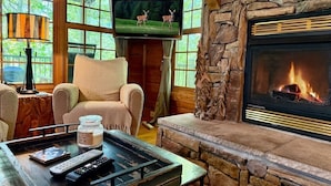 A cozy living room with a stone fireplace, a television mounted on the wall, and a comfortable seating area. - Boulder Lodge - The Perfect Mountain Escape in Banner Elk near Winery & Hiking (Banner Elk)