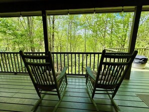 Eine Holzterrasse mit zwei Schaukelstühlen, die auf einen bewaldeten Bereich ausgerichtet sind.