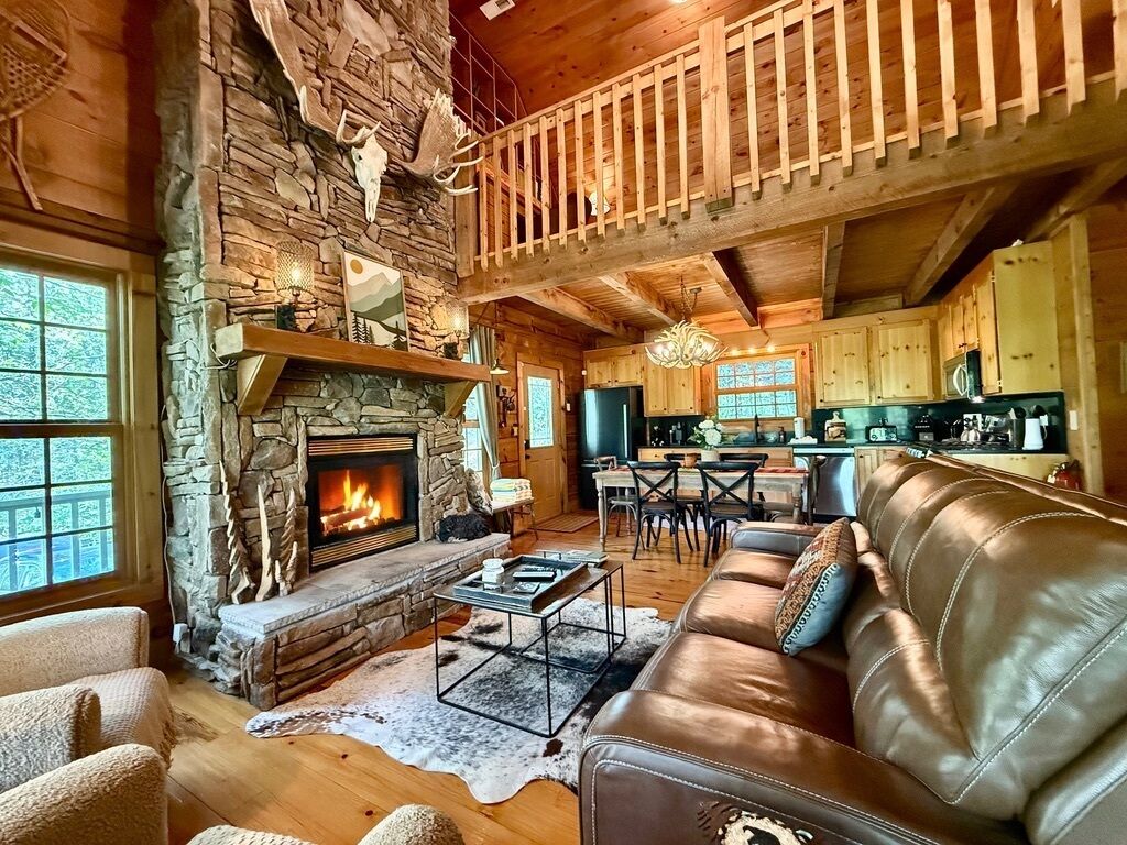 A cozy cabin interior with a stone fireplace, leather sofa, and a dining area.