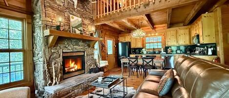 A cozy cabin interior with a stone fireplace, leather sofa, and a dining area.