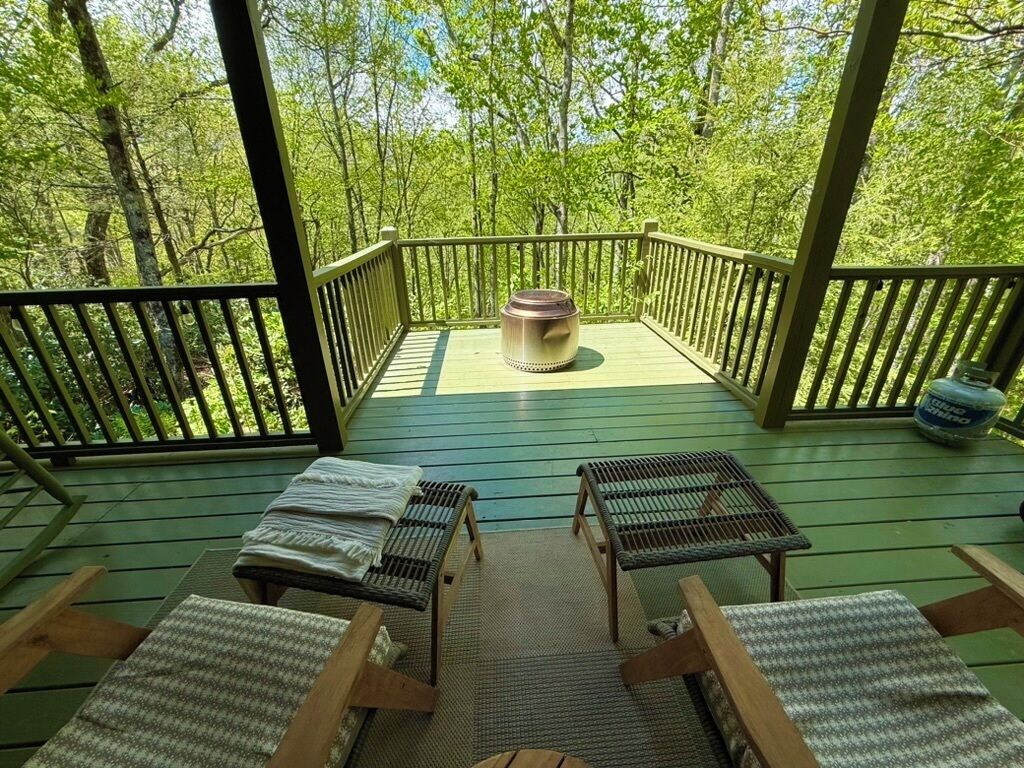 A covered outdoor deck with wooden railings, a central fire pit, and seating areas.