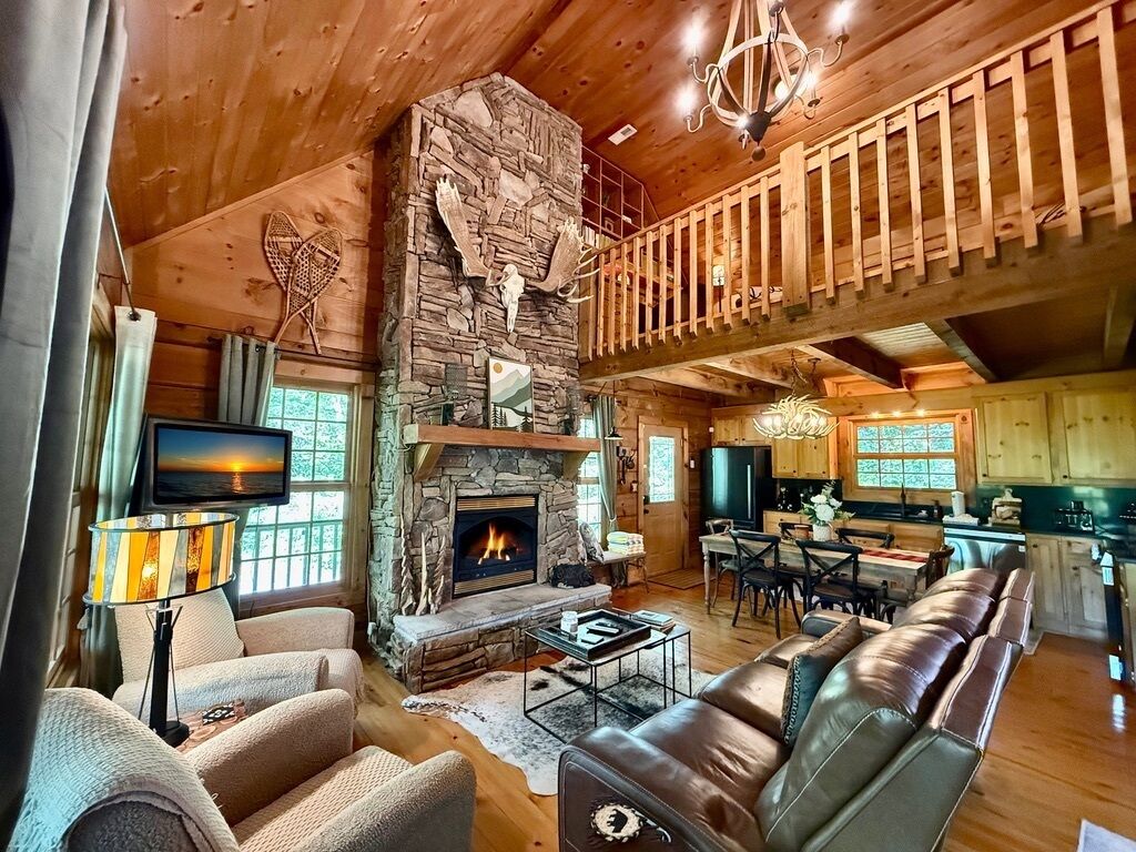 A cozy cabin interior with a stone fireplace, leather sofa, dining area, and a balcony.