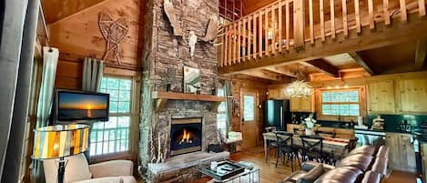 A cozy cabin interior with a stone fireplace, leather sofa, dining area, and a balcony.