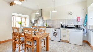 Een moderne keuken met een eettafel, stoelen, een wasmachine en een klok aan de muur.