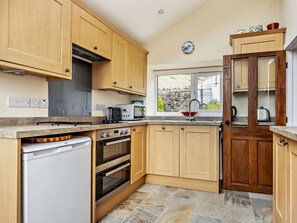 A kitchen with wooden cabinets, a built-in oven, a dishwasher, and a window with a view of the outside. - 1 Bed in Penrith (oc-91812) (Ullswater)