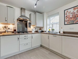 A modern kitchen with white cabinets, a stainless steel range hood, and a window with blinds. - 3 Bed in Buxton (oc-91785) (Buxton)