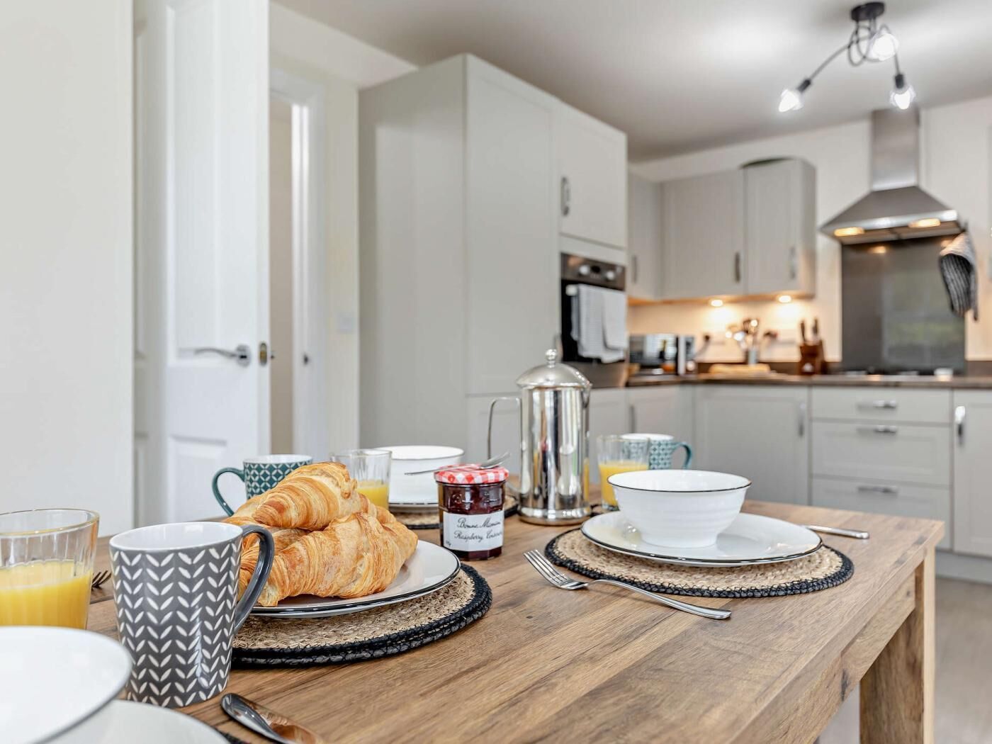 A breakfast table with croissants, a coffee pot, and a glass of orange juice.