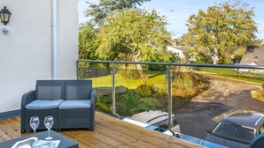 Ein Balkon mit Gartenmöbeln, Blick auf eine Straße und ein geparktes Auto.