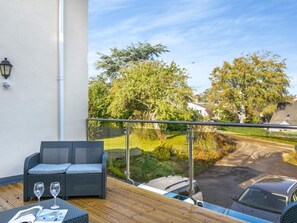Ein Balkon mit Gartenmöbeln, Blick auf eine Straße und ein geparktes Auto.