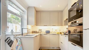 A compact kitchen with white cabinets, a built-in oven, and a window with a view of greenery. - 2 Bed in Poole (oc-91757) (Poole)