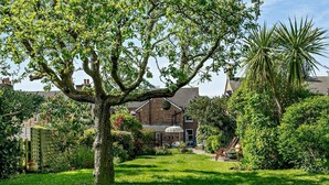 A well-maintained garden with a large tree, a lawn, and a brick house in the background. - 2 Bed in Poole (oc-91757) (Poole)