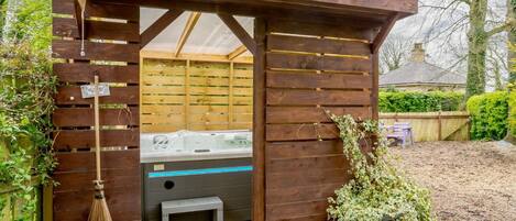 A wooden outdoor hot tub area with a bench and a broom.