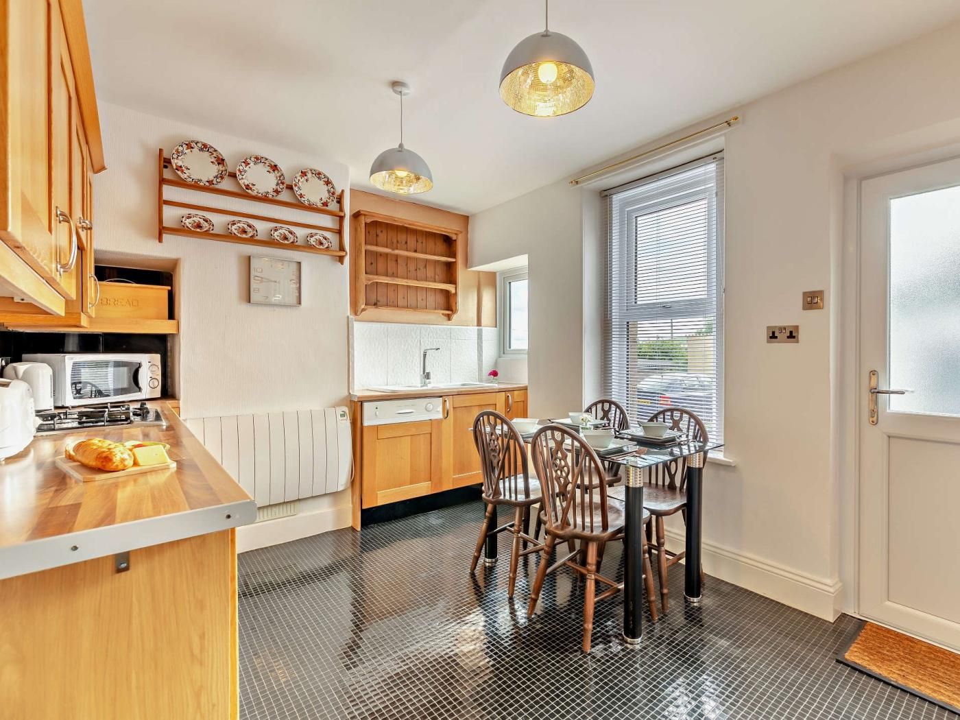 Et kompakt køkken med spiseplads, træskabe, en mikrobølgeovn og et vindue med skodder.